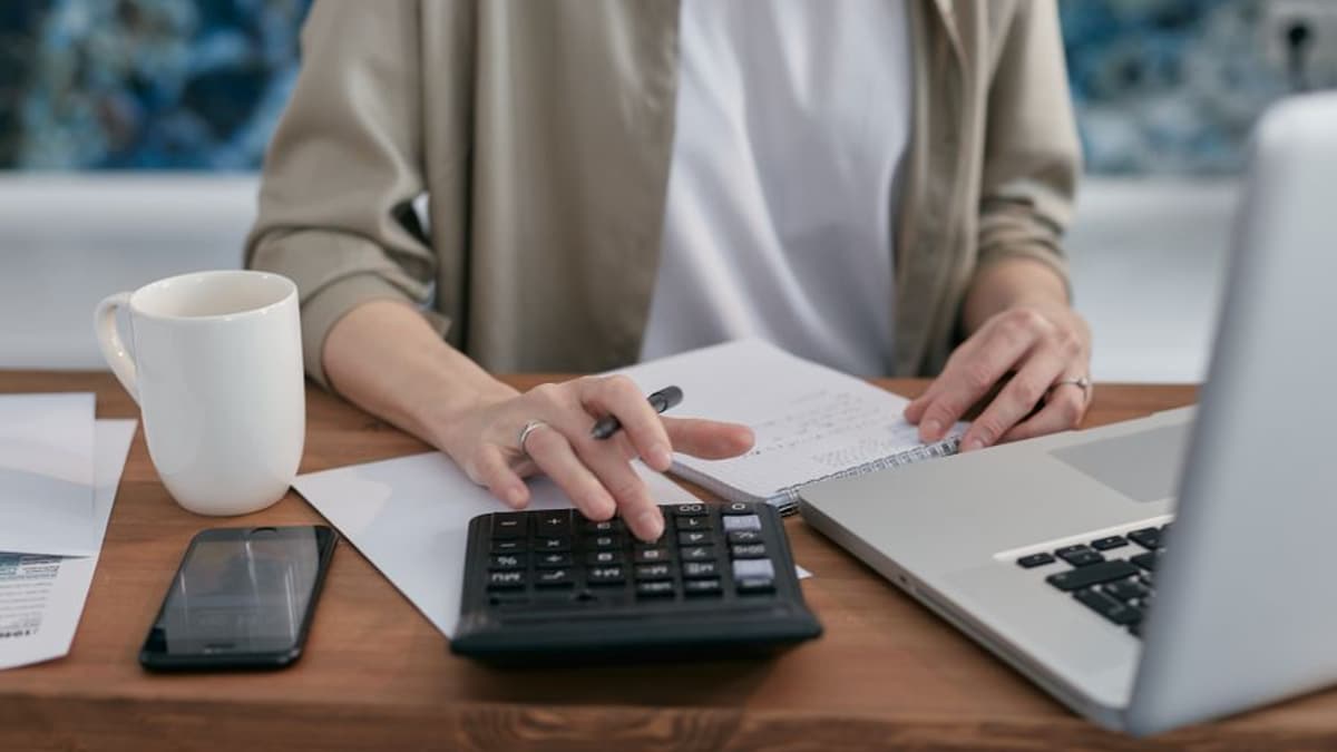 Mãos usando calculadora ao lado de notebook e caderno em uma mesa de escritório