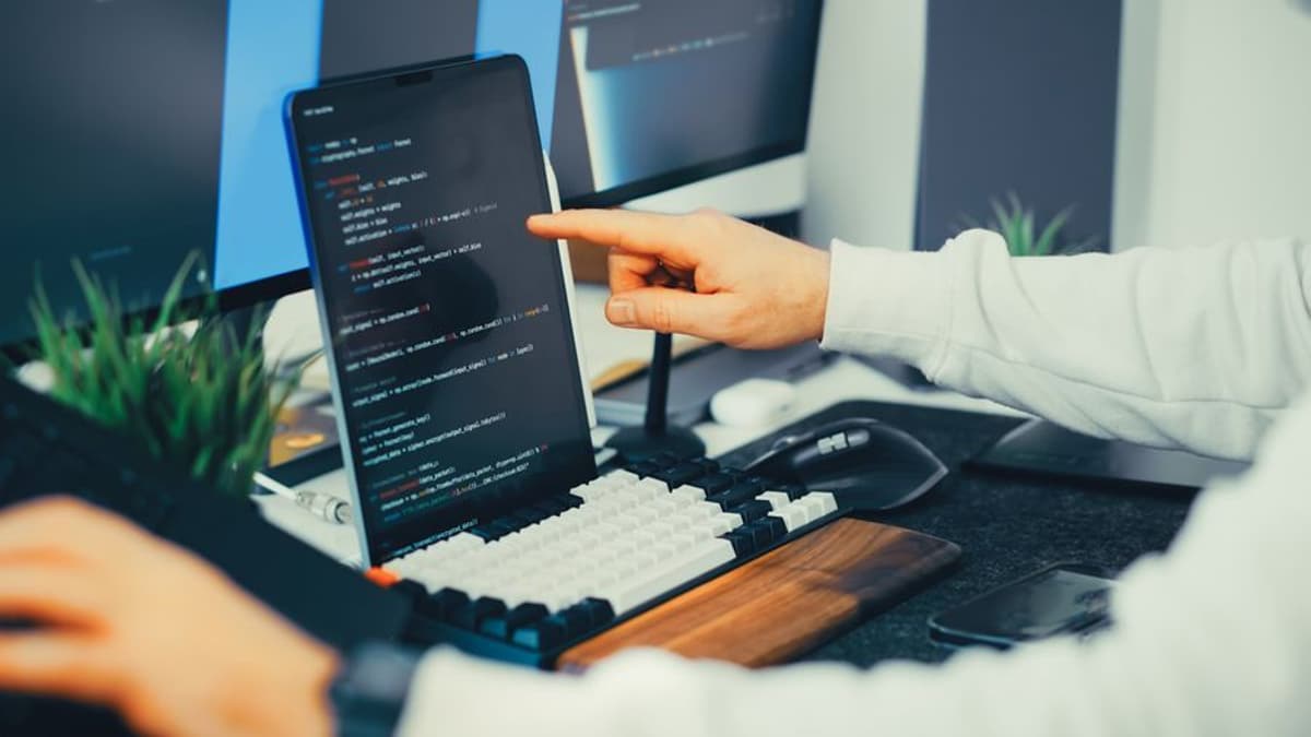 Pessoa apontando para código em uma tela ao lado de um teclado